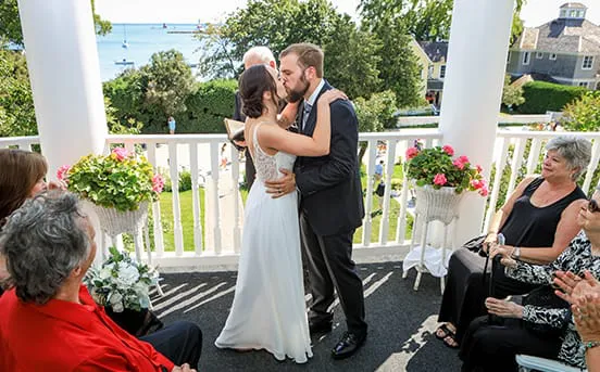 A bride and groom kissing on the front porch at their wedding.